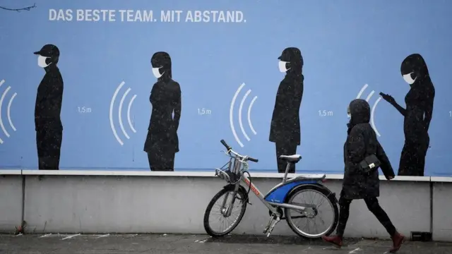 اUne femme passe devant un panneau en Allemagne qui dit : "La meilleure équipe garde des distances."