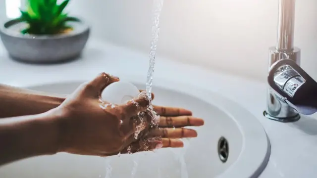 Mãos sob torneira e segurando sabonete