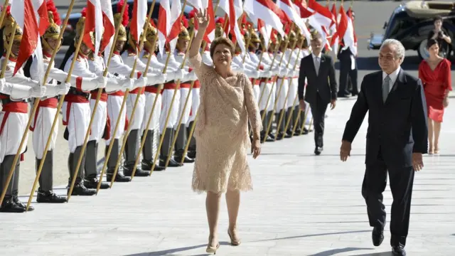 Dilma Rousseff e Michel Temer sorriem caminhandocomo jogar dardoscorredor formado por dragões (guardas)