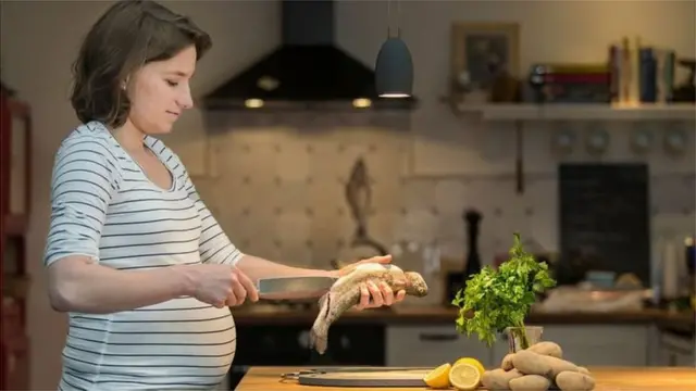 Une femme enceinte, préparant du poisson dans la cuisine.