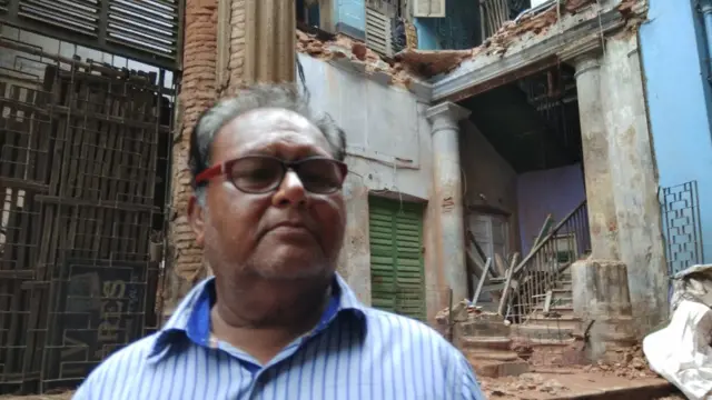 ভেঙ্গে পড়া বাড়ির সামনে পরিবারের এক আত্মীয় পবনলাল সাউ