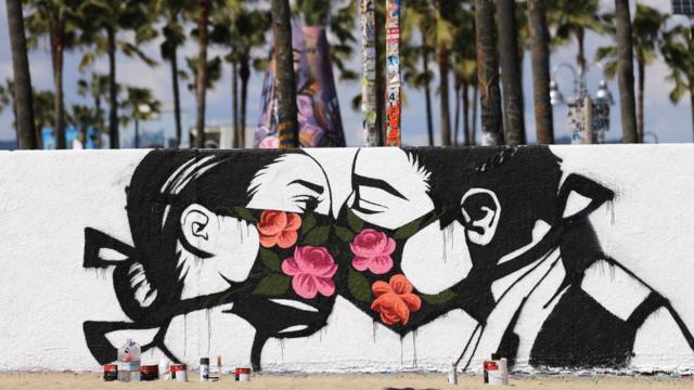 Grafite do artista Pony Wave retratando duas pessoas se beijando enquanto usam máscaras, em Venice Beach, Califórnia, EUA - março de 2020