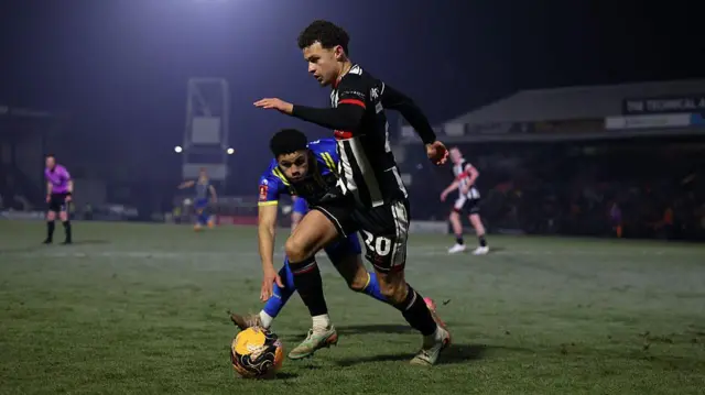 Dos jugadores corren hacia un balón en un campo oscuro.
