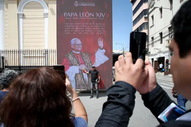 Человек позирует для фотографий рядом со светодиодным экраном, на котором изображен папа Лев XIV, перед собором Чиклайо 10 мая 2025 года в Чиклайо, Перу. Лев XIV был избран Конклавом 8 мая 267-м понтификом. Родившийся в Чикаго 14 сентября 1955 года как Роберт Фрэнсис Прево, нынешний Папа много лет работал в Перу, прежде чем был назначен епископом Чиклайо на период с 2014 по 2023 год