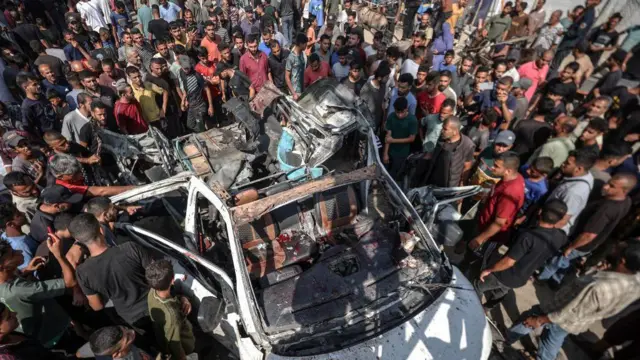 فلسطینی‌ها اطراف یک خودرویی که در دیرالبلح هدف حمله اسرائیل قرار گرفت جمع شده‌اند