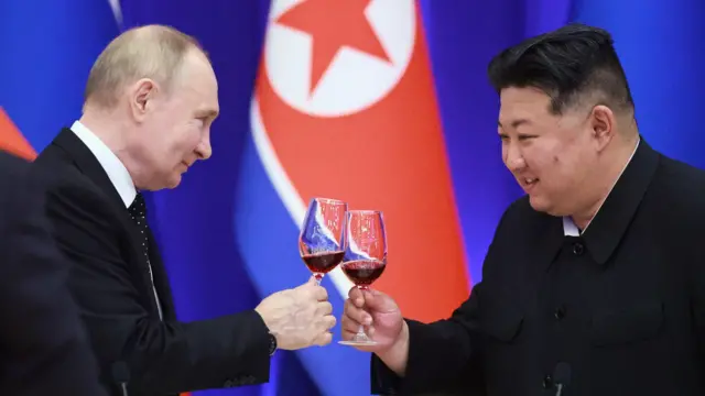 O presidente da Rússia, Vladimir Putin, e o líder norte-coreano Kim Jong Un sorriem durante um brinde com vinho tinto, com uma bandeira da Coreia do Norte ao fundo