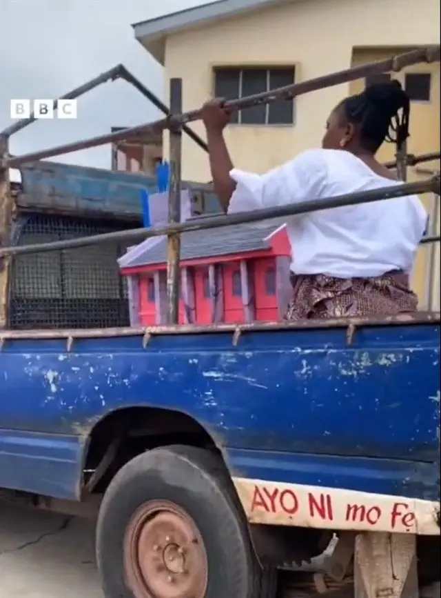 Boluwatife Adewuyi to fi akara oyinbo mọ sọọsi katidira gbe keeki naa sinu ọkọ akẹru alawọ buluu, oun naa joko ti akara oyinbo naa, o wọ buba funfun ati iro alawọ eeru, o si ko irun suku to se soke ori rẹ.