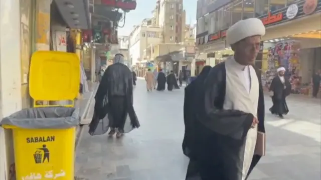 په نجف کې یوه واټ چې دواړو غاړو ته یې هټۍ دي، او یو شمېر لارویان، د څلورو دیني عالمانو په ګډون، په کې د تېرېدو په حال کې دي.