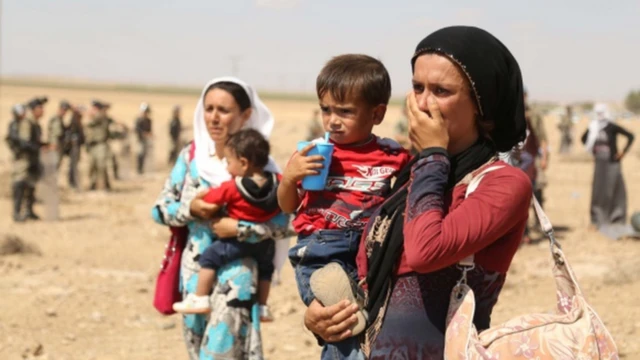 İki kadın, kucaklarında çocuklarla bir şey izliyor.