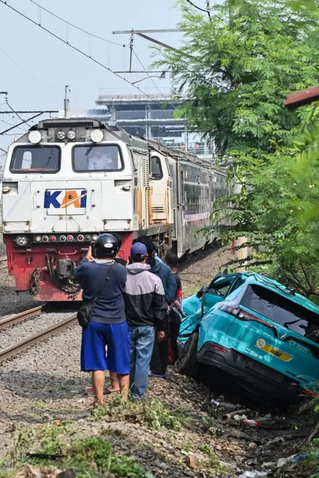 Một đoàn tàu đường dài chạy ngang qua chiếc taxi hãng Vinfast của công ty Green SM Indonesia bị hư hỏng liên quan đến vụ tai nạn xảy ra vào đêm 27/4 (ảnh chụp hôm 28/4/2026)