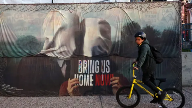 Dečak vozi bicikl pored postera u kojem se zove na oslobađanje talaca 