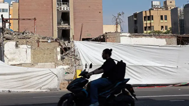 موتور سواری در حال عبور از جلوی خانه ای تخریب شده در ایران