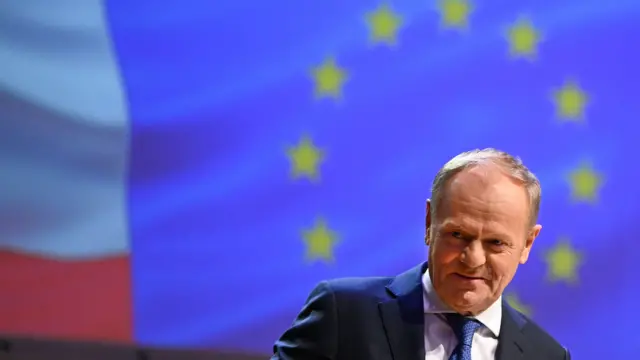 Na zdjęciu Donald Tusk stoi przed flagą Unii Europejskiej.
