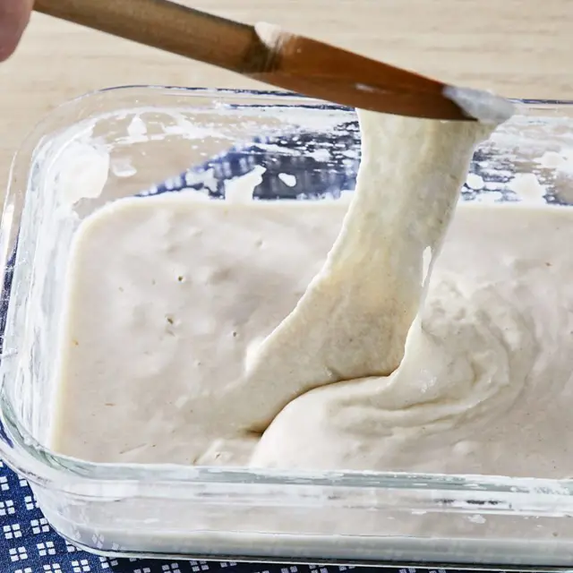 Massa de pão em um recipiente de vidro, sendo retirada por uma colher