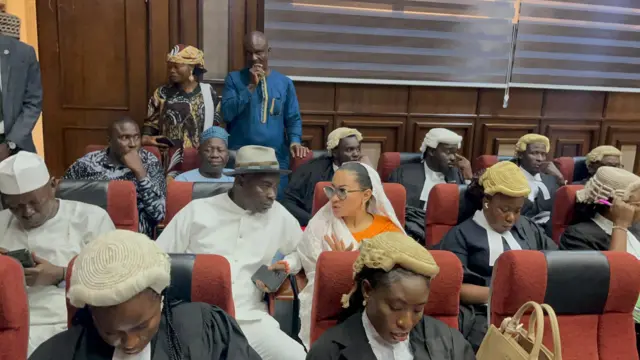 Lawyers wit wigs and Senator Natasha sit for middle dey tok wit her husband