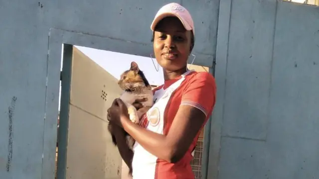 Mwanamke anayeitwa Victoria Soo, amesimama mbele ya mlango wa buluu, amevalia shati jekundu na kofia huku amembeba paka wake 'Ella' wakiangalia kamera. Paka huyu alifariki ghafla na kumuacha na majonzi.