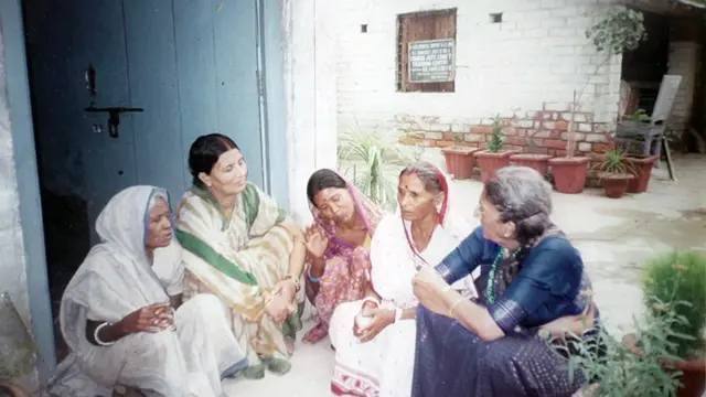 Anila, vestida aquí con un sari verde, blanco y dorado, escucha a un grupo de parteras, todas sentadas en el suelo, que le hablan. Fotografía de archivo de los años 90.