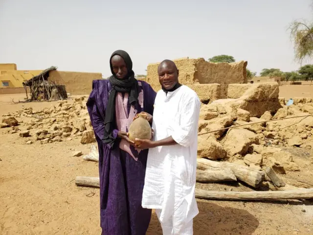 Le Dr Mamarane Seck-Enseignant chercheur à l'IFAN avec le chef de village de Coppé (Nord du Sénégal). Derrière eux un bâtiment en banco tombé en ruine et une maison qui ressemble à une terrasse au fin fond.