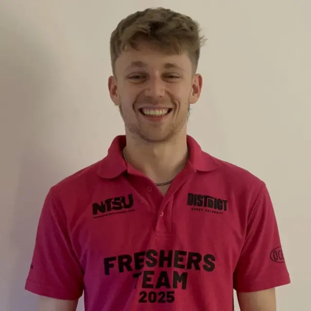 一位男子穿著印有「2025年新生團隊」(Freshers Team 2025)字樣的粉紅/紅色 T 恤,面帶微笑的特寫鏡頭。