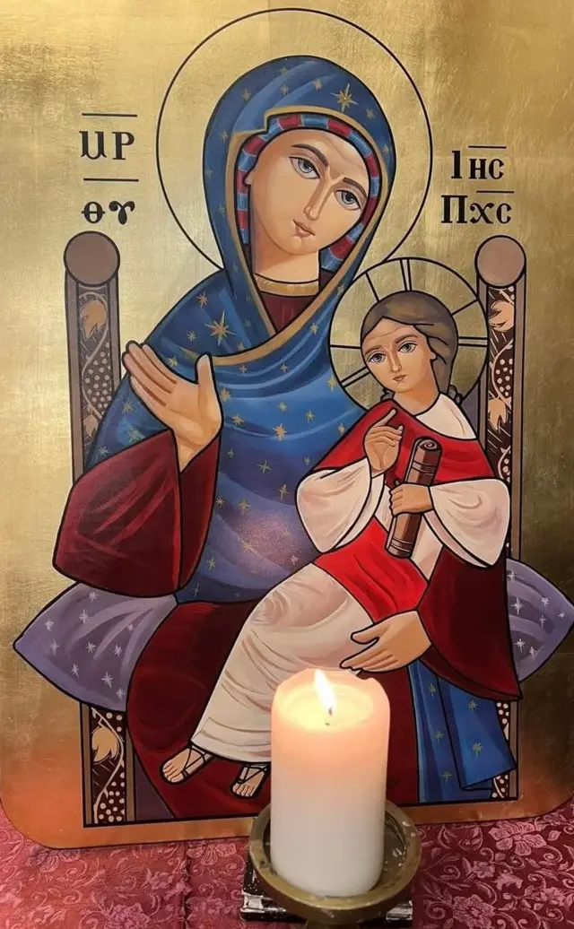 أيقونة قبطية تمثل القديسة العذراء مريم جالسة وهي تحمل الطفل يسوع المسيح، وأمامهما شمعة مشتعلة 