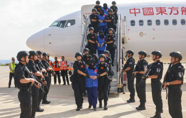 မြန်မာကနေတရုတ်ကို အွန်လိုင်းလိမ်လည်မှုတရားခံလွှဲပြောင်းမှု တစ်ခုကိုတွေ့ရစဥ်၊ အပြာရောင်ဝတ်တရားခံတွေကို ခေါင်းစွပ်ပြီး လေယာဥ်ပေါ်က ခေါ်ချလာချိန် တရုတ်လက်နက်ကိုင်လုံခြုံရေးတွေ ထူထပ်စွာချထားပါတယ်။