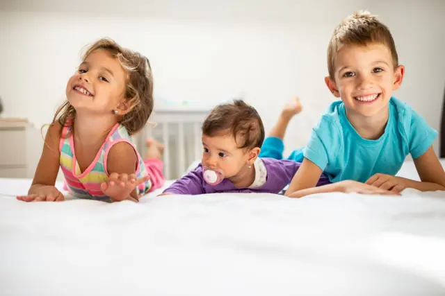 Três crianças de diferentes idades sobre uma cama
