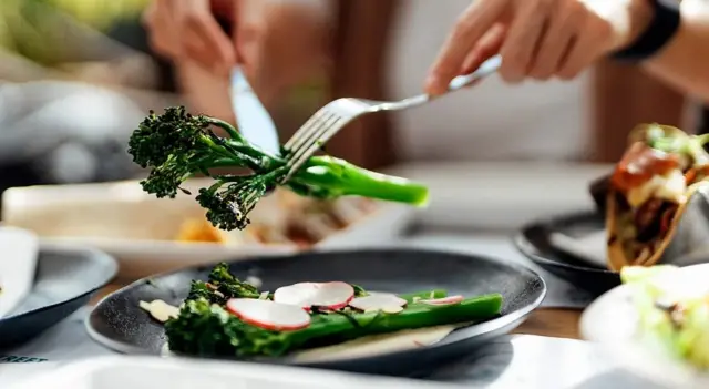 Gros plan sur les mains d'une femme mangeant une salade fraîche sur une table garnie de légumes bio.