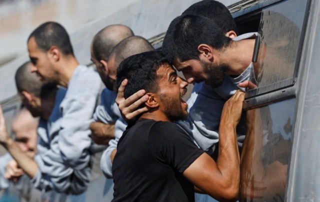 Bir adam otobüs penceresine uzanmış, pencereden de yakını sarkıyor, kucaklaşıyorlar.