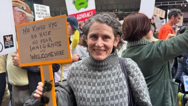 Beth Zasloff döviz tutuyor ve objektife bakıyor. Dövizde "Krallara Hayır, Nefrete Hayır, Korkuya Hayır, Göçmenlere Kapımız açık" yazıyor.