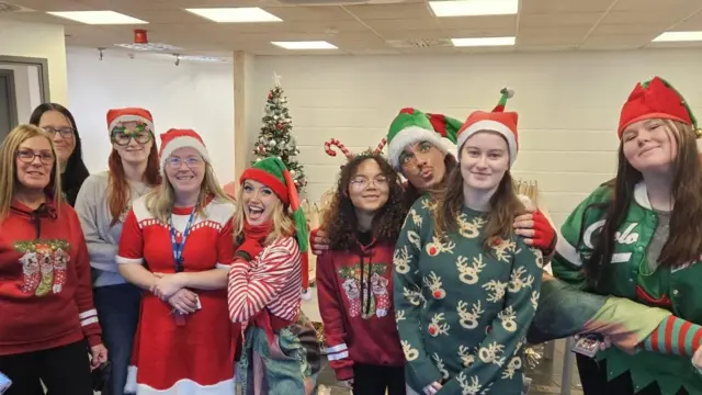 Un grupo de voluntarios vestidos con ropa festiva y gorros de Papá Noel sonríen a la cámara.