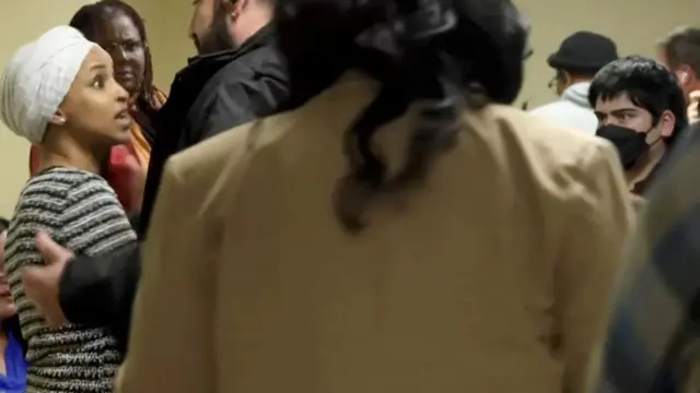 في صورة ثابتة من مقطع فيديو، يظهر أحد أفراد الأمن وهو يمنع النائبة الأمريكية إلهان عمر (ديمقراطية من مينيسوتا) من دخول قاعة اجتماعات عامة بعد أن تهجم عليها رجل، في مدينة مينيابوليس بولاية مينيسوتا الأمريكية