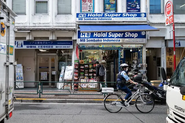 Seorang petugas polisi bersepeda melewati sebuah toko serba ada di distrik Okubo, satu pemberhentian di utara metro Shinjuku, di Tokyo pada 12 Juni 2026, sebuah lingkungan yang dikenal dengan komunitas imigrannya yang besar, termasuk penduduk Korea, Asia Tenggara, dan Asia Selatan.