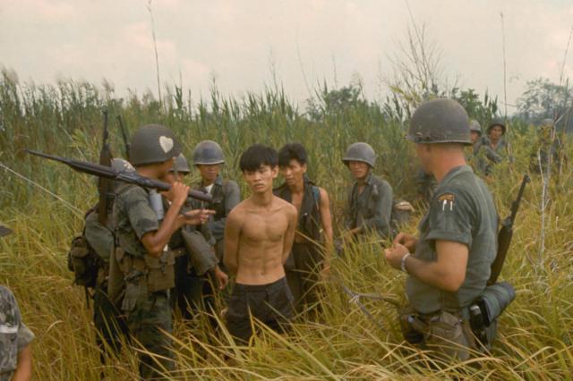 Um grupo de soldados do exército sul-vietnamita e um soldado americano com dois suspeitos vietcongues capturados.