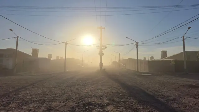 Rua de terra, nuvem de pó e o sol do amanhecer