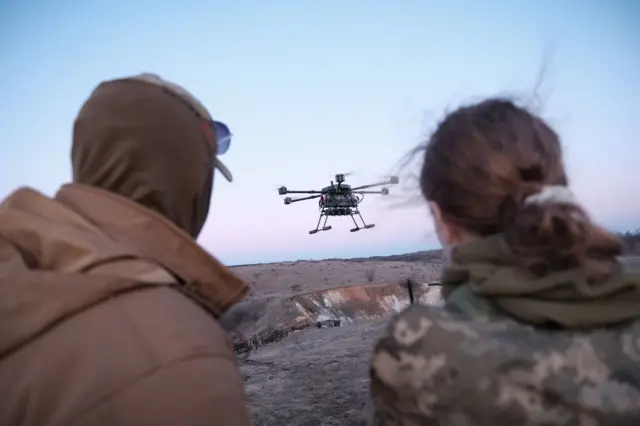 Хлопець із дівчиною в камуфляжі на тлі квадрокоптера, що злітає