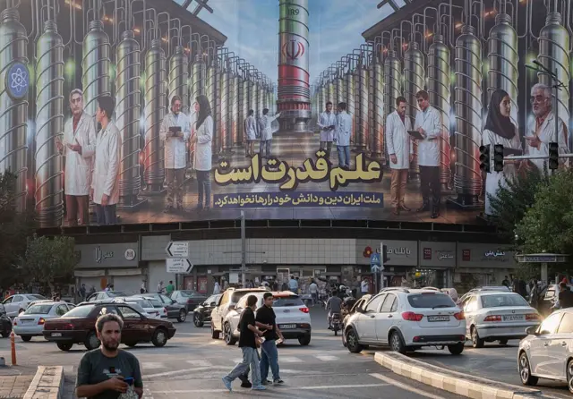 ইরানের একটি সরকারি ভবনে ব্যানার ঝুলছে যেখানে নাতাঞ্জ পারমাণবিক কেন্দ্রের প্রতীকী ছবি, ইসরায়েলের হামলায় নিহত বিজ্ঞানীদের ছবি আছে এবং ফার্সি ভাষায় লেখা 'বিজ্ঞানই শক্তি'