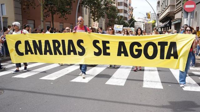 Manifestantes caminan por una avenida con una pancarta que dice: Canarias se agota