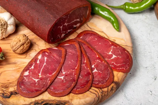 bir tahta üzerine sıralanmış dilim pastırmalar ve yeşil biber, sarımsak ve kabuklu ceviz