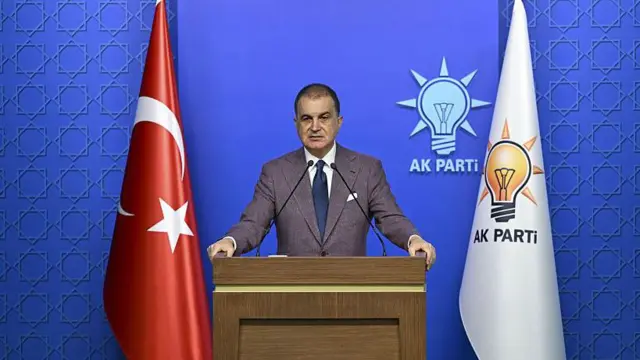 AKP Sözcüsü Ömer Çelik bir kürsüde konuşurken arkasında Türkiye ve AKP bayrakları yer alıyor
