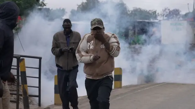 Two men dey waka, one cover nose as tear gas smoke dey dia back