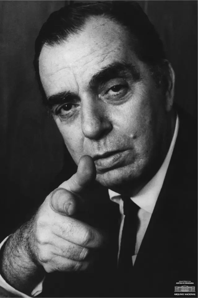 Rodrigues posando para retrato com olhar desafiador, apontando para a câmera