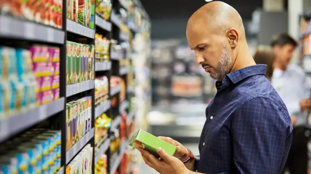 Homem olha para o rótulo de um produto em um corredor no supermercado