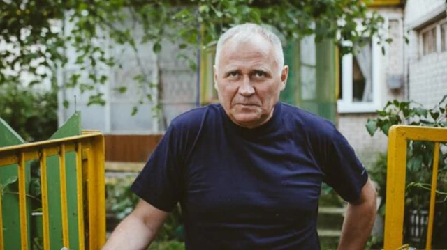 Николай Статкевич в синей футболке позирует у ворот дачи или деревенского дома