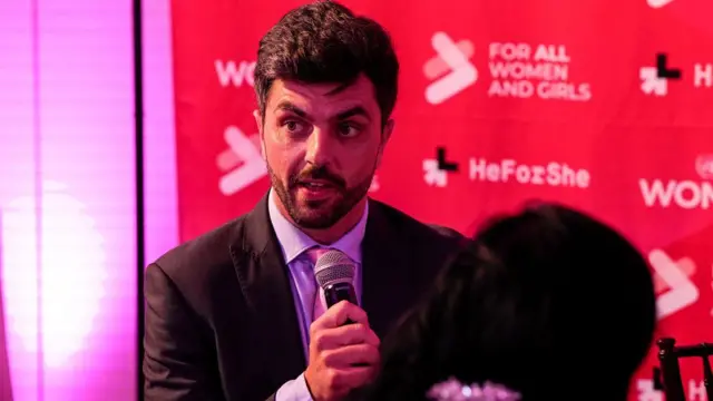 Will Adolphy, de barba corta bien cuidada, con un saco oscuro, camisa azul y corbata rosada, habla al micrófono durante la conferencia HeForShe (ÉlPorElla) de la ONU