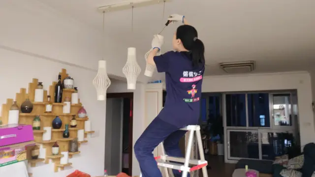 一位女性坐在梯子上，手拿螺丝刀拆卸灯胆