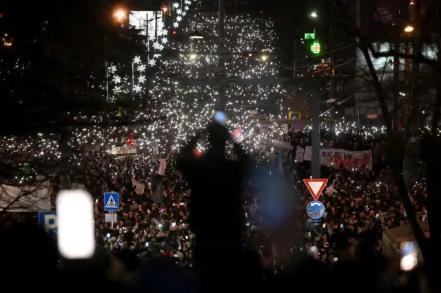 Bir adam, 22 Aralık 2024'te Belgrad şehir merkezinde düzenlenen protestoya katılan binlerce öğrenci ve vatandaşın fotoğrafını çekiyor.