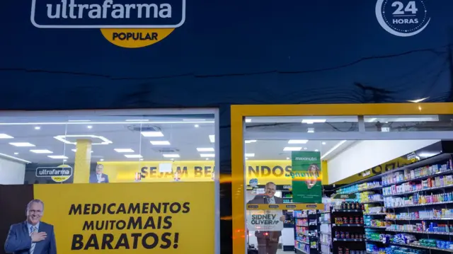 Fachada de uma farmácia Ultrafarma, com a vitirne com medicamentos e uma foto de Sidney Oliveira fazendo propaganda. 