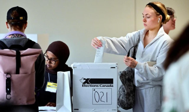 Kanada halkı 28 Nisan'da sandık başına gitti. Eşofmanlı sarışın bir kız, oy atıyor. Sandık başında görevli başörtülü bir kadın var.