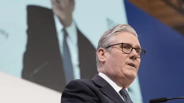 壇上で演説するスターマー氏。背後の壁には、ステージの正面からの映像が映し出されている