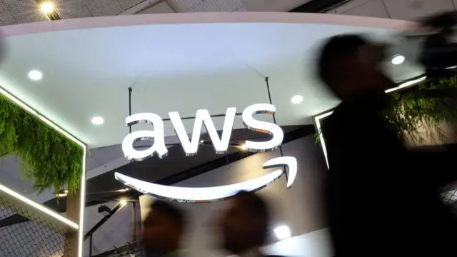 AWS logolu duvarın önünde geçen insan silüetleri 